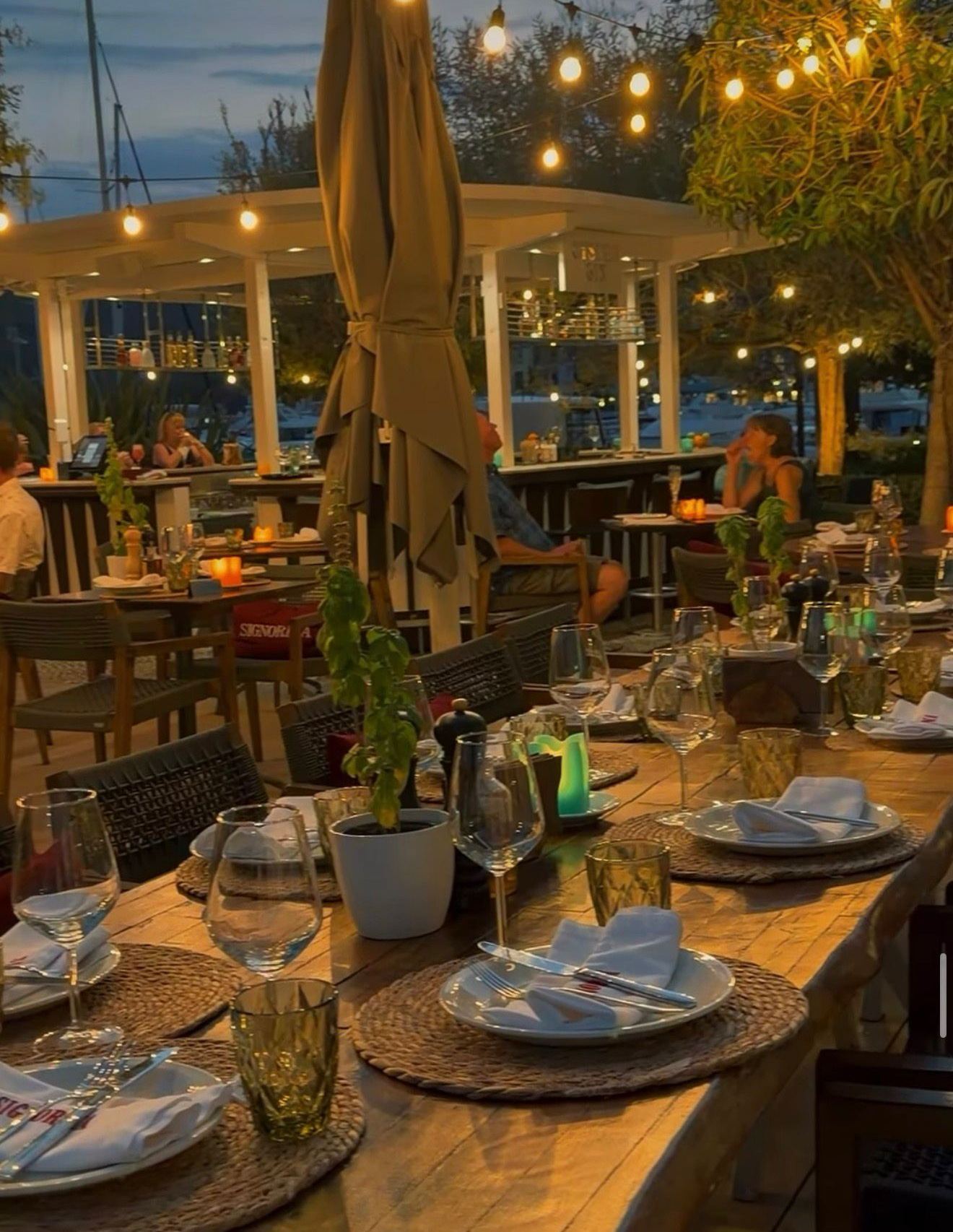 Restoran Signorina na Luštici: terasa u suton, postavljeni stolovi pod lampicama i marina iza